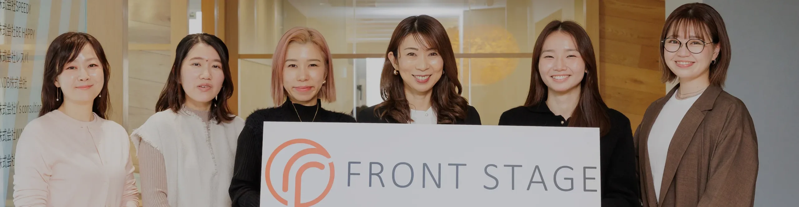 「FRONT STAGE」のロゴパネルを囲み、華やかな笑顔で並ぶ6人の女性チームメンバー。