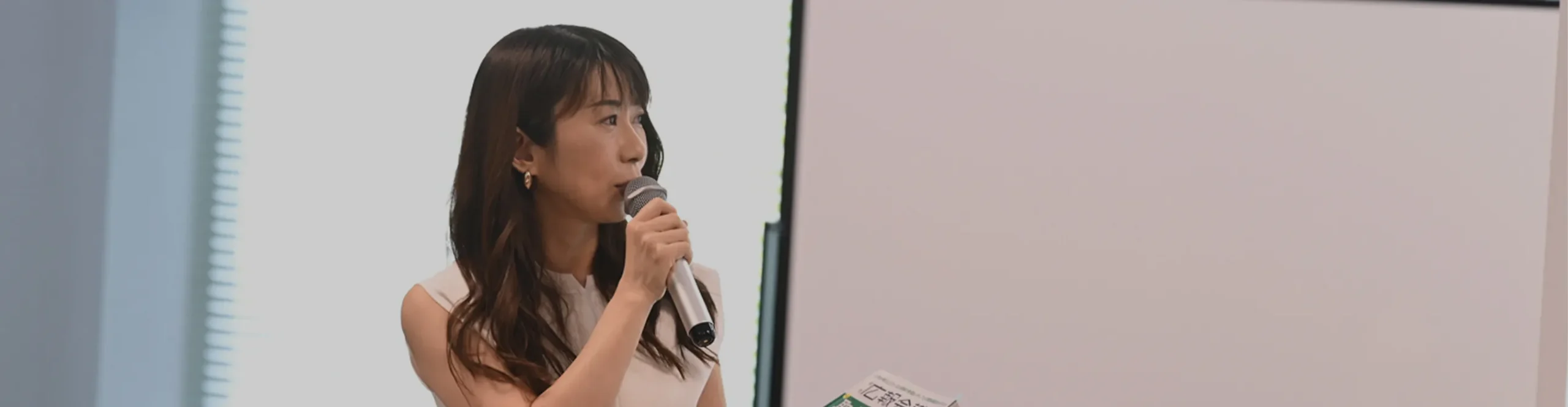 セミナーや記者発表会にて、マイクを手に持ち真剣な表情で登壇する女性。